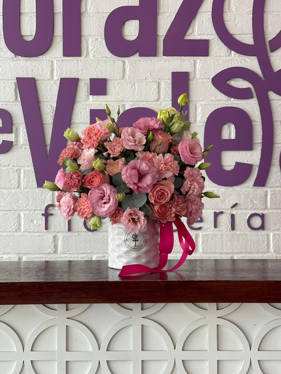 Arreglo de flores rosas en base blanca con listón rosa